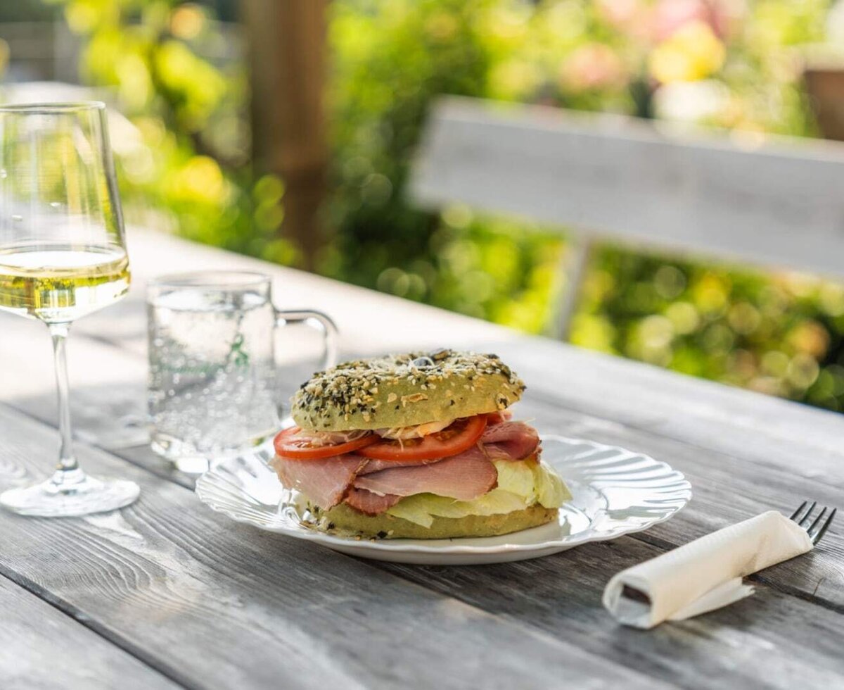 Bagel sandwich, white wine, and water on a wooden outdoor table at the Haus.