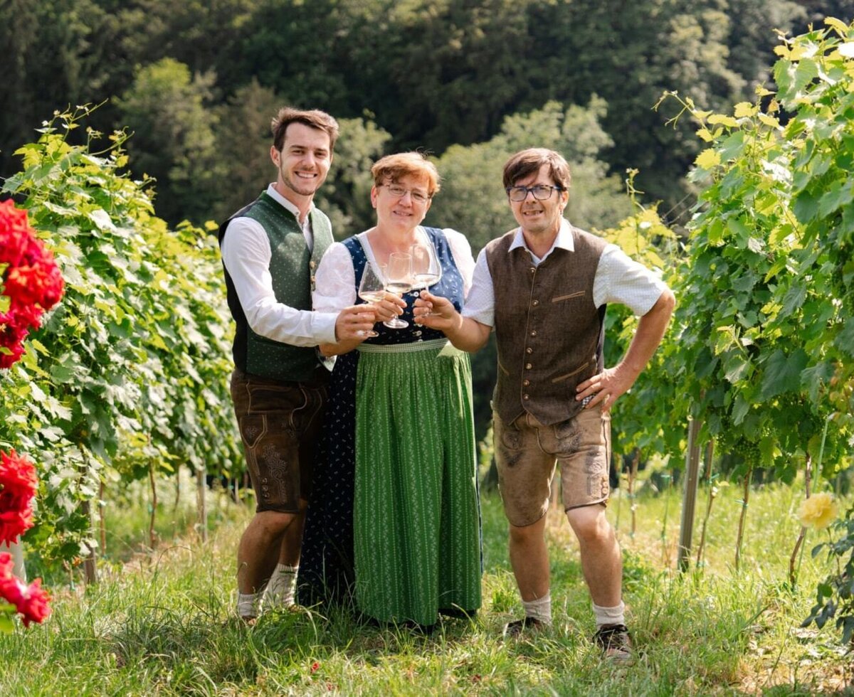 The hosts of the Haus in a vineyard holding wine glasses.
