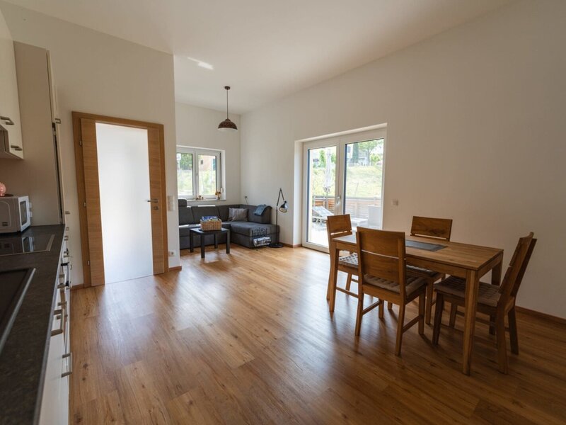 Open-plan living area in the house featuring a kitchen counter, a dining table for four, a living area with a sofa, and access to the terrace.