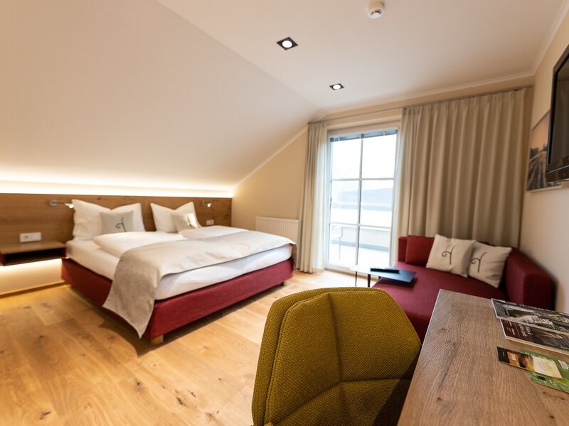 A farmhouse bedroom featuring a double bed, a sofa, a desk, a television, and access to a balcony.