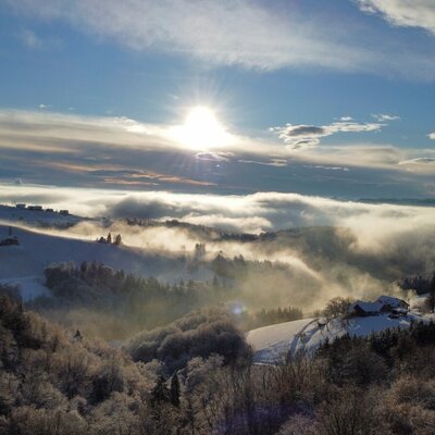Winter view from the Haus of a landscape with snow-covered hills, fog, and sunshine.