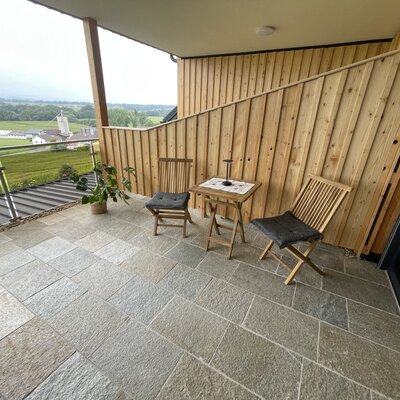 Balcony at the farmhouse featuring stone tiles, a wooden privacy wall, two chairs, a small table, and a view of the countryside.