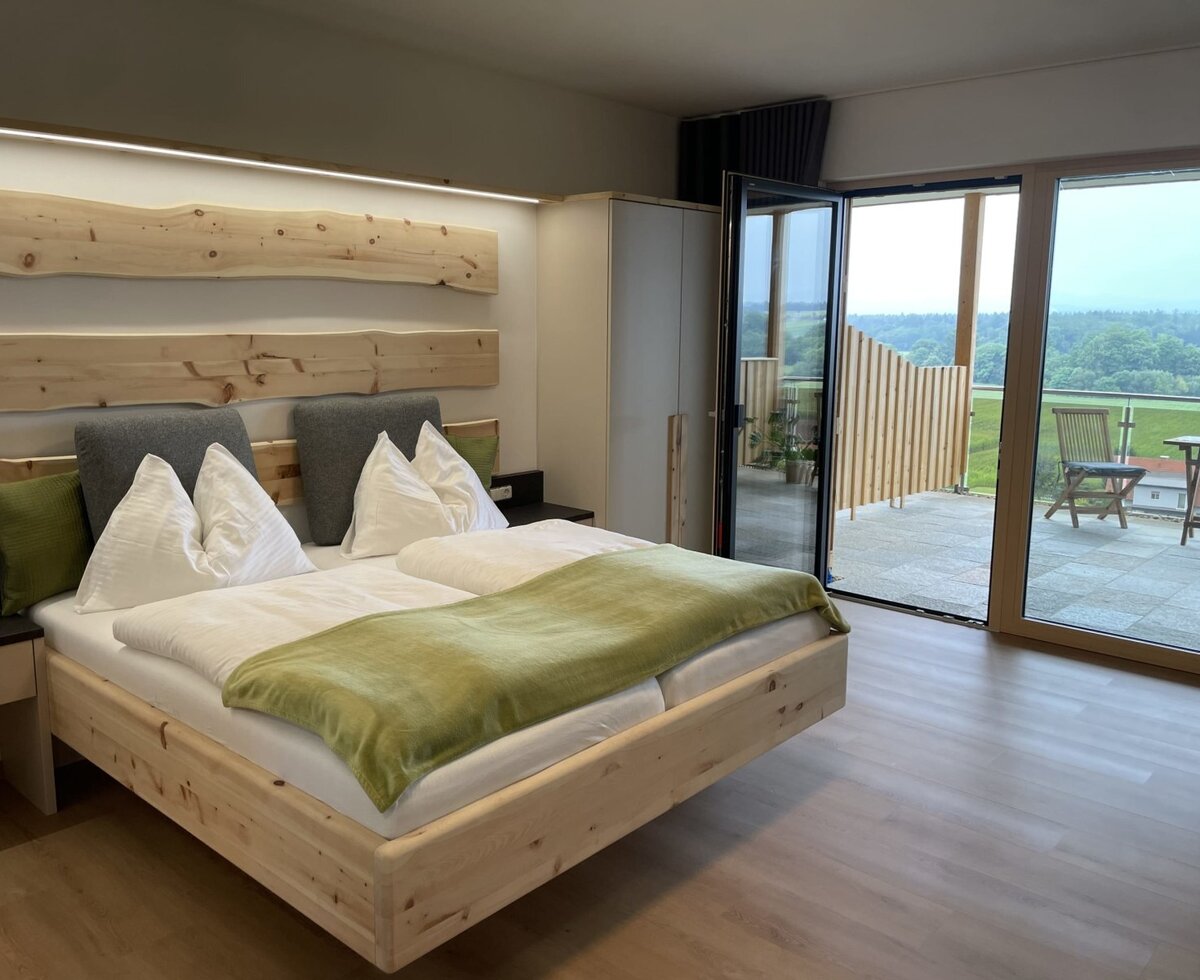 Double bedroom in the farmhouse with a wooden bed and a wardrobe, offering direct access to a balcony with outdoor seating and a view of the surrounding landscape.
