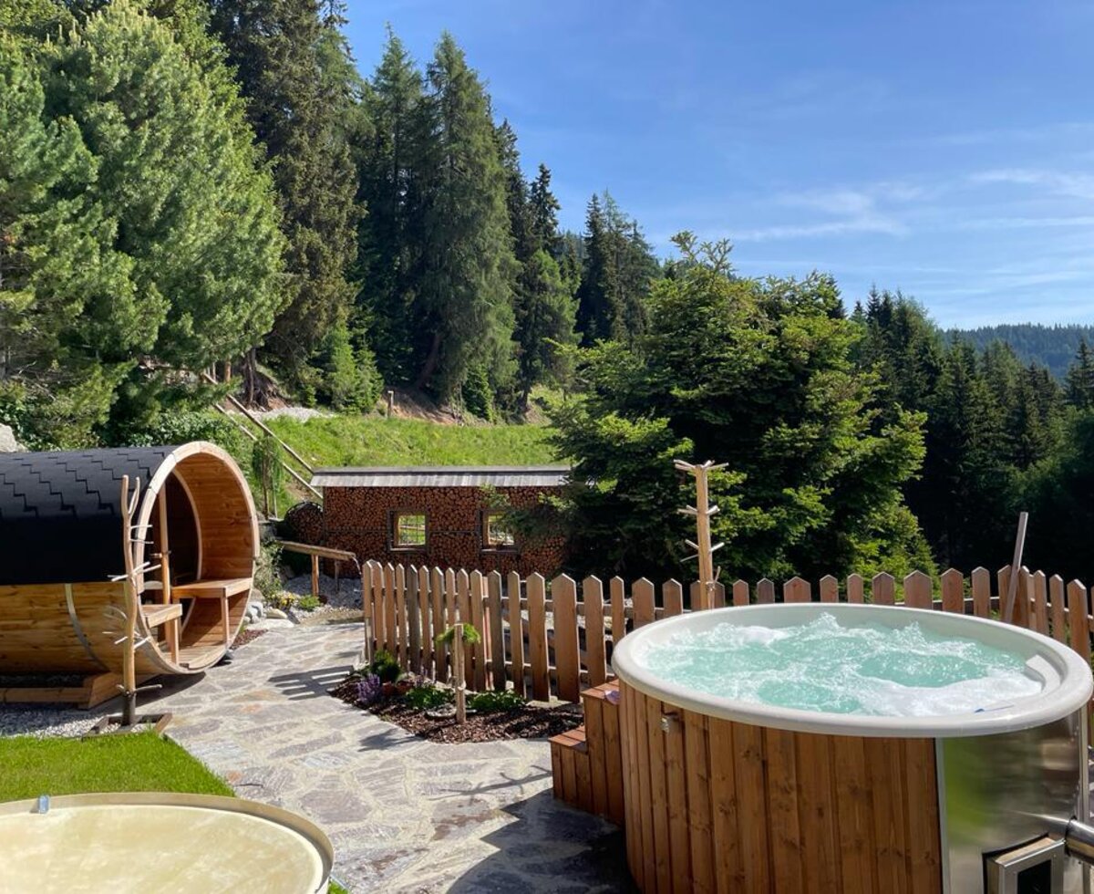 The farmhouse features an outdoor hot tub and a barrel sauna for guest use, surrounded by the forest.