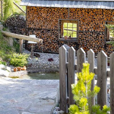 Wood storage structure at the Bed and Breakfast, featuring windows, a small pond with a wooden water spout, and a stone path.