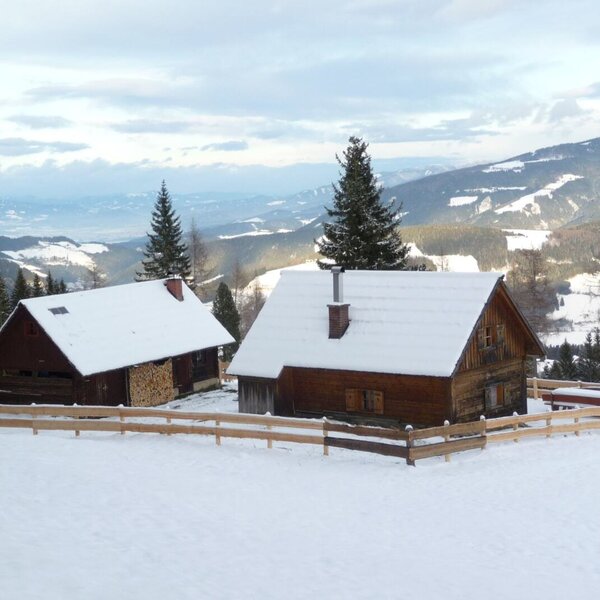 The wood-clad farmhouse and its adjacent building, covered in snow, with views of the surrounding mountains.