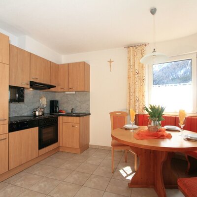 The apartment kitchen in this Farm House includes wooden cabinets, cooking appliances, a dining table with bench seating, and windows with mountain views.