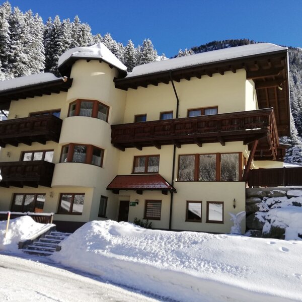 The multi-story Farm House exterior, featuring balconies and surrounded by snow with a mountain backdrop.