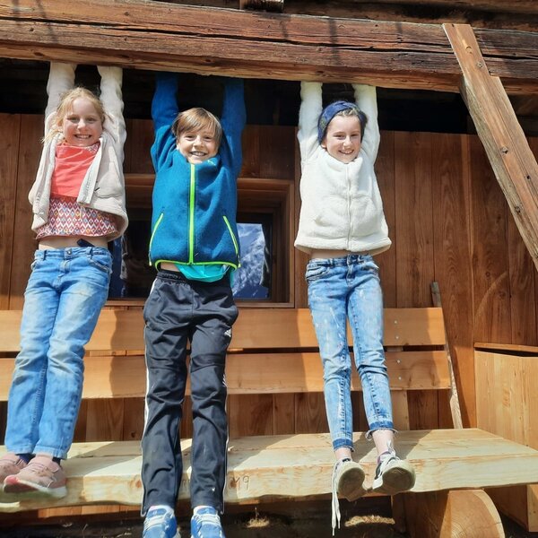 Children playing on a wooden beam at the farmhouse, with a wooden bench in the outdoor area.