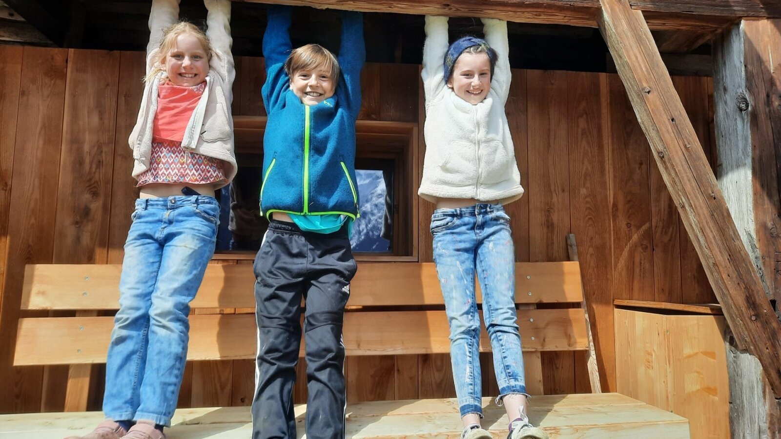 Children playing on a wooden beam at the farmhouse, with a wooden bench in the outdoor area.