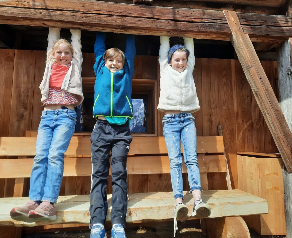Children playing on a wooden beam at the farmhouse, with a wooden bench in the outdoor area.