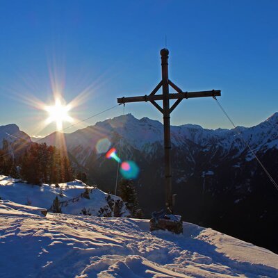 The snowy mountain landscape surrounding the Farm House, featuring a summit cross and bright sunrise over the peaks.