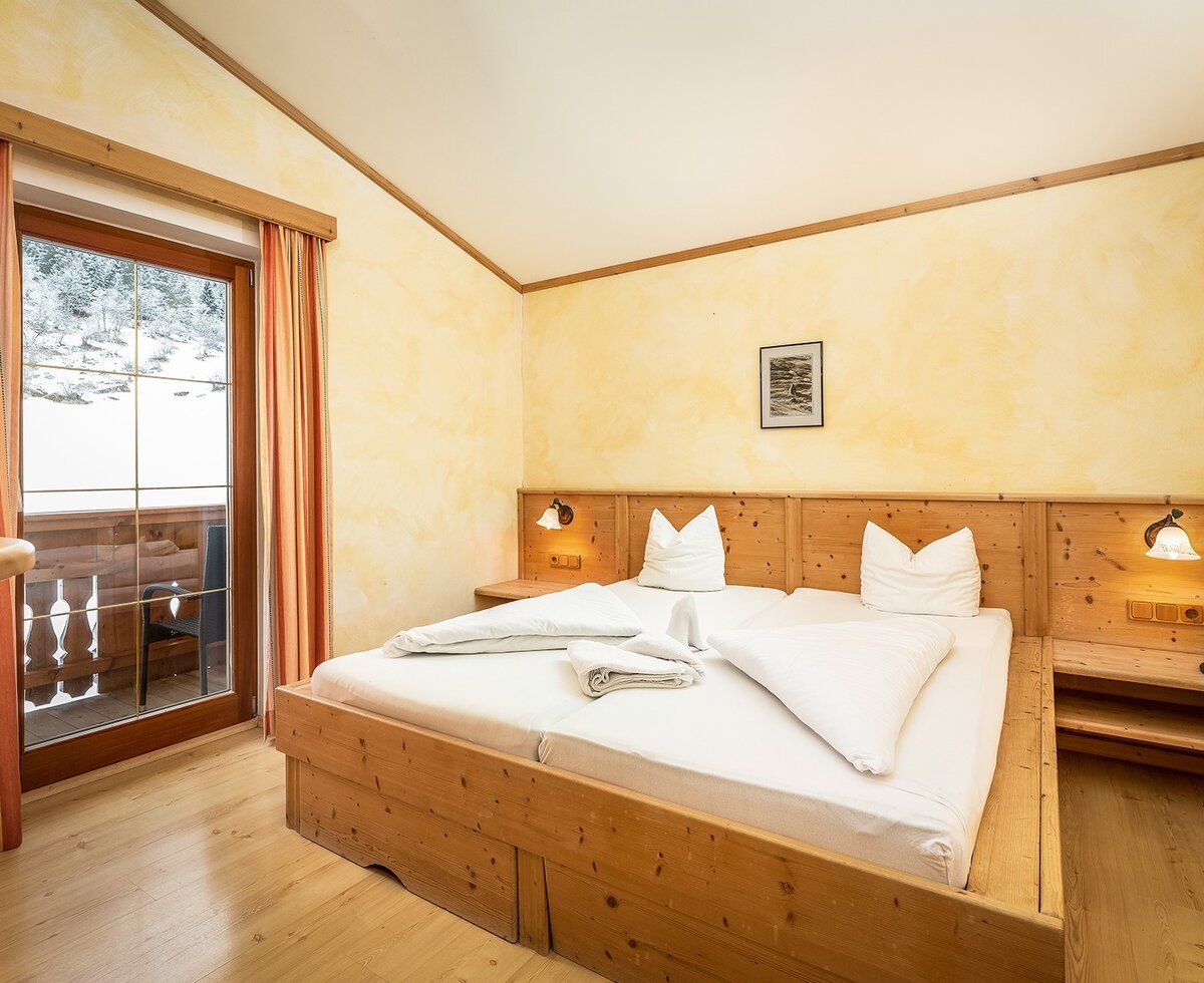 Double bedroom in the Farm House featuring a wooden XL double bed, bedside tables with a telephone, and balcony access with views of a snowy landscape.