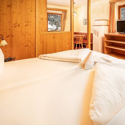 Bedroom area in the Farm House featuring an XL bed, telephone, and TV, with a view of the snowy mountains and an adjoining dining space.