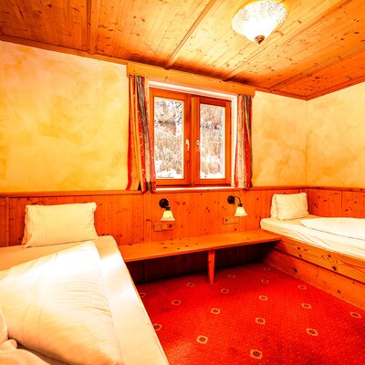 Bedroom in the Farm House with two single beds, wooden walls and ceiling, and a red patterned carpet.