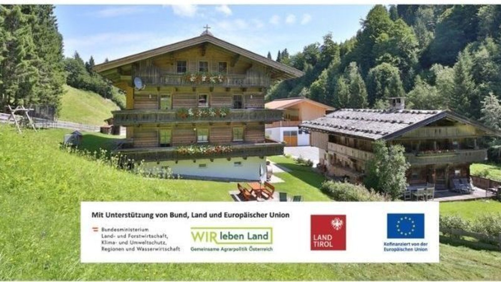 The inviting farmhouse surrounded by green mountain meadows, featuring traditional wooden balconies and a well-kept garden area.