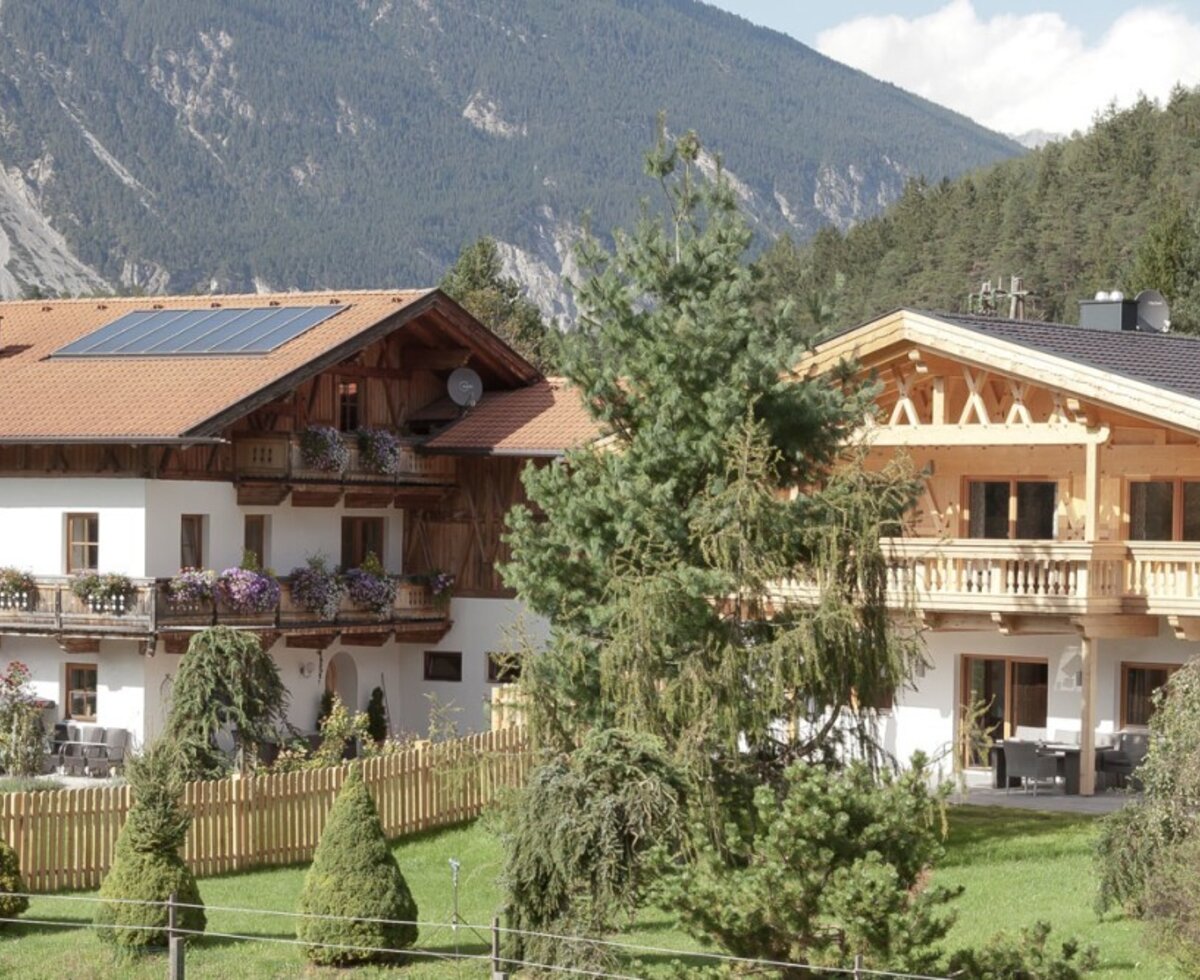 The charming apartments in a traditional alpine design, surrounded by a green garden and a scenic mountain backdrop.