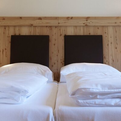 Inviting double bed in the apartment featuring crisp white bedding, a rustic wooden headboard panel, and warm reading lights.
