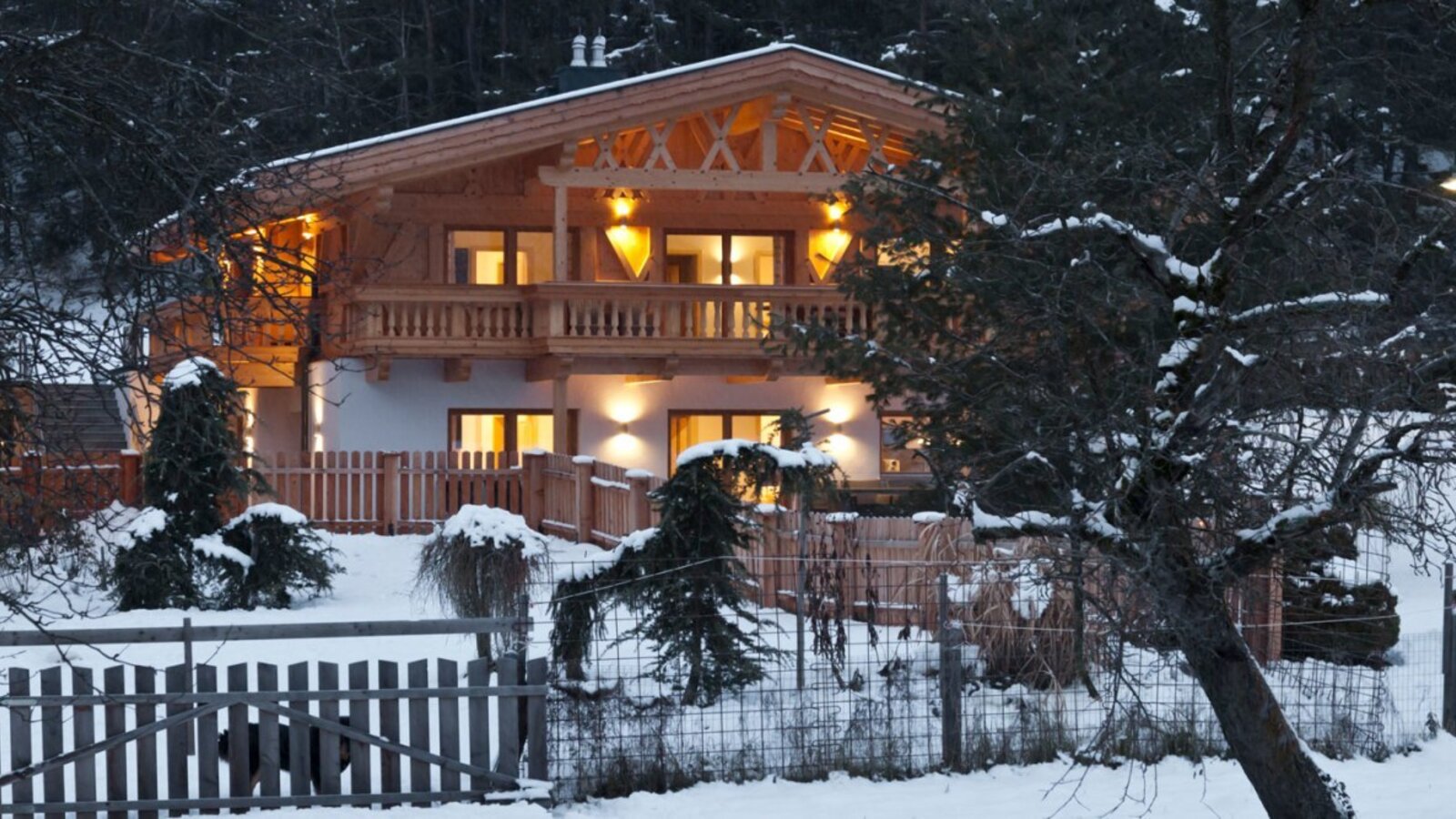 The charming apartment building warmly lit at dusk, nestled in a snowy winter landscape.