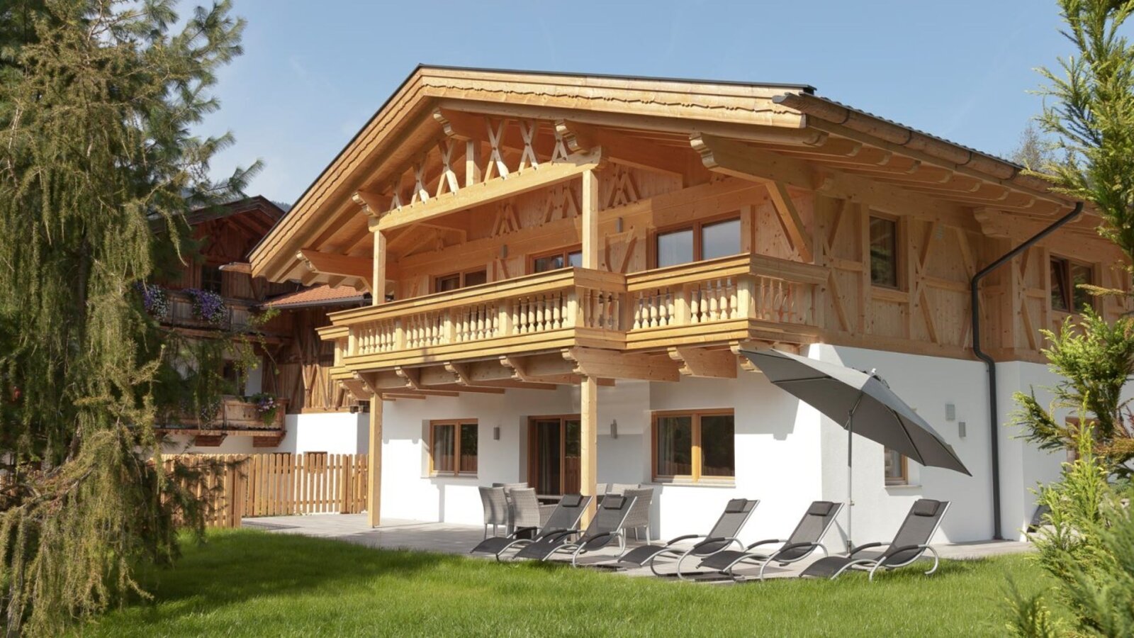 The inviting apartments featuring a wooden facade, a sunny terrace, and comfortable loungers in the green garden.