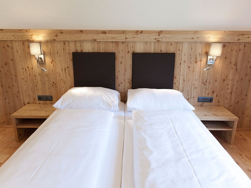 A cozy double bed in the apartment featuring a rustic wooden headboard wall, light bedside tables, and inviting reading lamps.