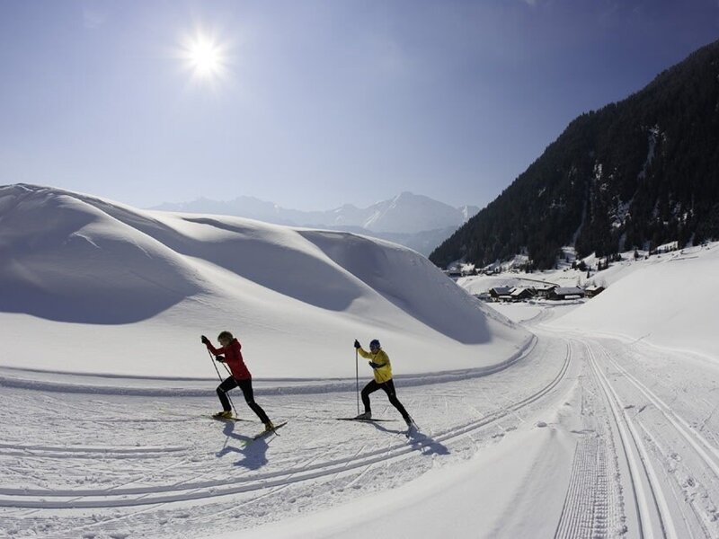 Cross-country skiing on a groomed track in a sunny, snowy mountain valley.