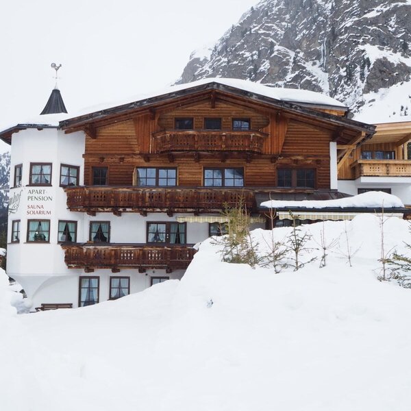 The Farm House exterior, featuring wooden balconies and signage for Apart Pension, Sauna, and Solarium, surrounded by a snowy mountain landscape.