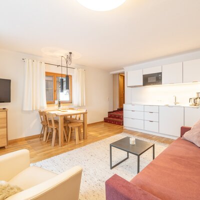 The apartment's main living area features a fully equipped kitchen with white cabinetry, a wooden dining table, and a lounge area with a sofa and television.