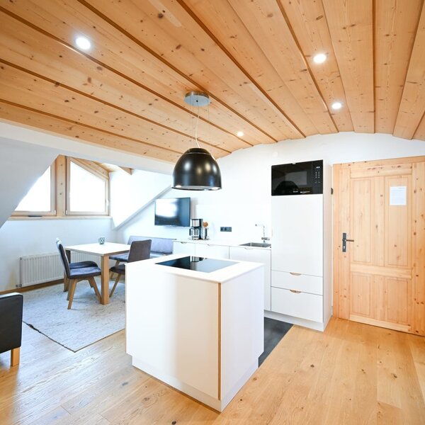 Open-plan living area of the apartment in the farmhouse, featuring a modern kitchen with an island, a dining area, a sofa, and a wooden ceiling.