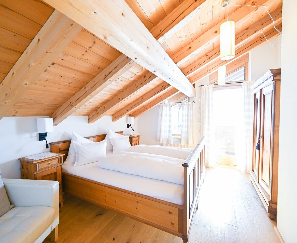Bedroom in the apartment of the farmhouse, featuring a pine wood double bed, exposed wooden beam ceiling, wardrobe, and a seating area.