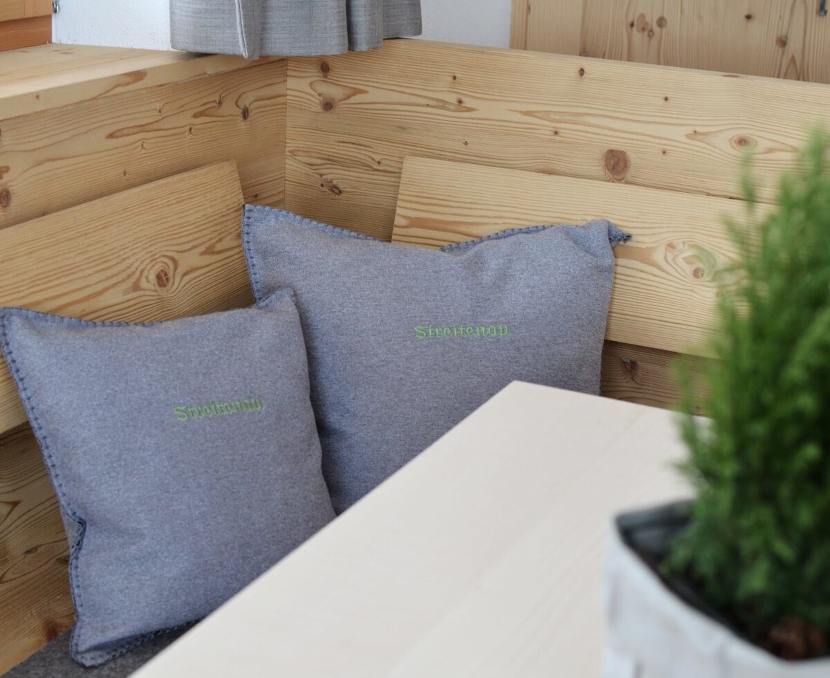 The farm house features a wooden corner dining bench with grey cushions and a light-toned table.