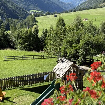 Children's playground with a slide and deck chairs on the lawn of the Bauernhof, offering views of the surrounding green fields and mountains.