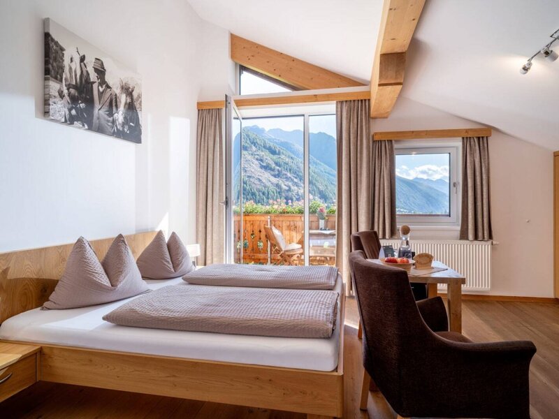 A bright double room at the farmhouse featuring rustic wooden furniture, a cozy seating area, and a balcony with scenic mountain views.