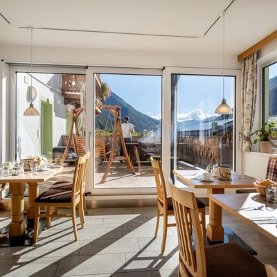 A sunlit breakfast room in the farmhouse featuring cozy wooden dining sets and beautiful mountain views through large glass doors.