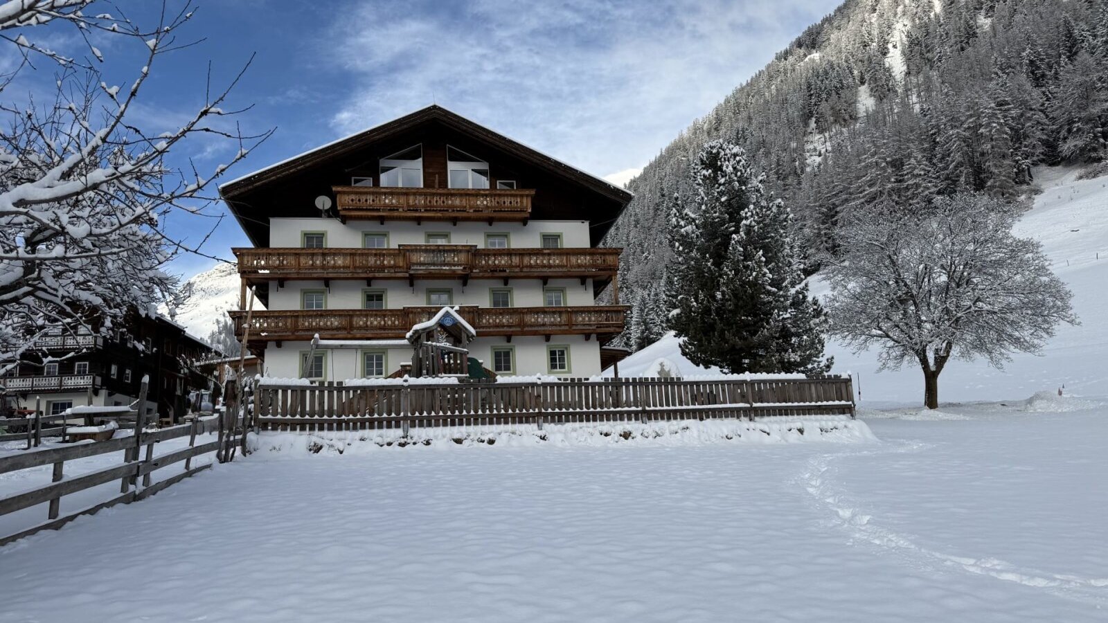 The inviting farmhouse surrounded by an idyllic, snow-covered winter landscape and forested mountain slopes.