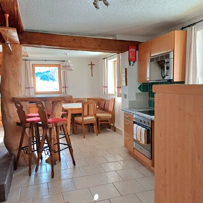 The Alpine Hut features a fully equipped kitchen with an oven and microwave, and a dining area with a table, bench seating, and bar stools.