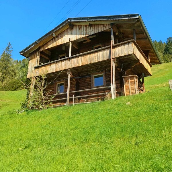 The exterior of the Alm, a two-story wooden building with a balcony on a green hillside.