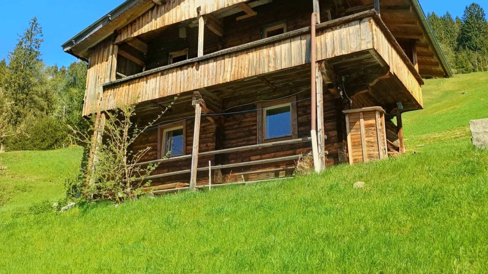 The exterior of the Alm, a two-story wooden building with a balcony on a green hillside.