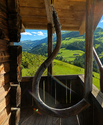 The alm's cozy wooden balcony featuring a unique rustic swing and scenic views of the lush green valley.