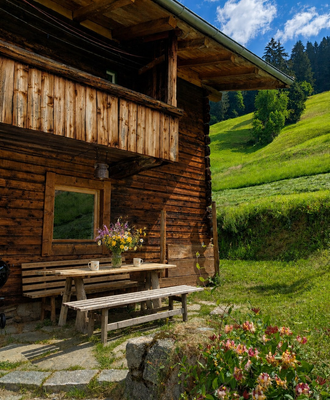 An inviting outdoor seating area in front of the rustic Alm, surrounded by lush green meadows.