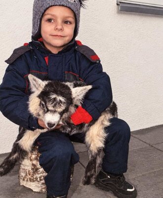 A young boy gently cradling a fluffy little lamb outside the apartments.