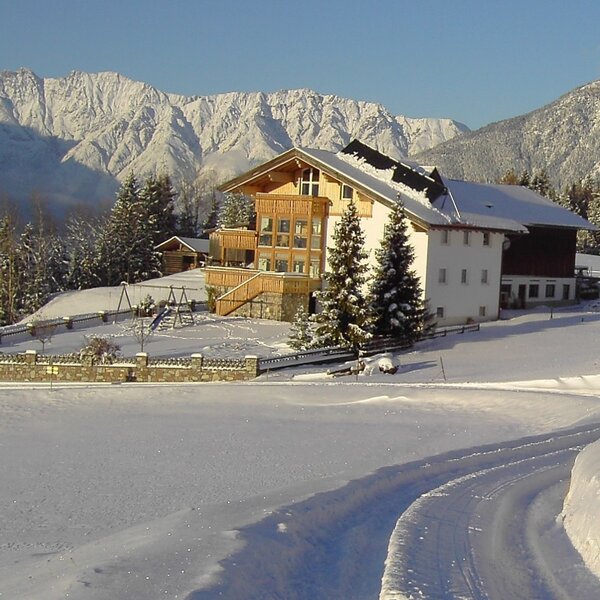 The Farm House exterior in winter, featuring a snow-covered playground and views of the surrounding mountains.