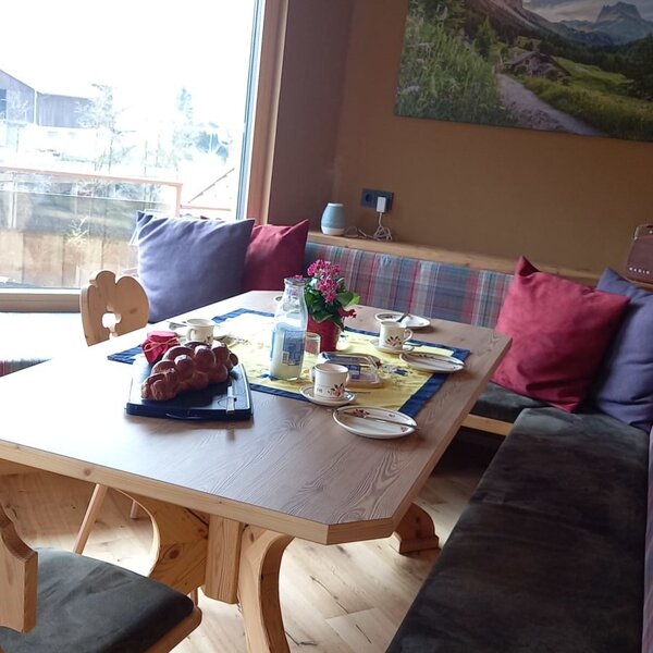 The farmhouse dining area features a wooden table, upholstered bench seating, and a large window, set up for breakfast.