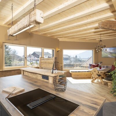 The farm house kitchen and dining area includes a modern induction hob, wooden furnishings, and large windows with views of the surrounding landscape.