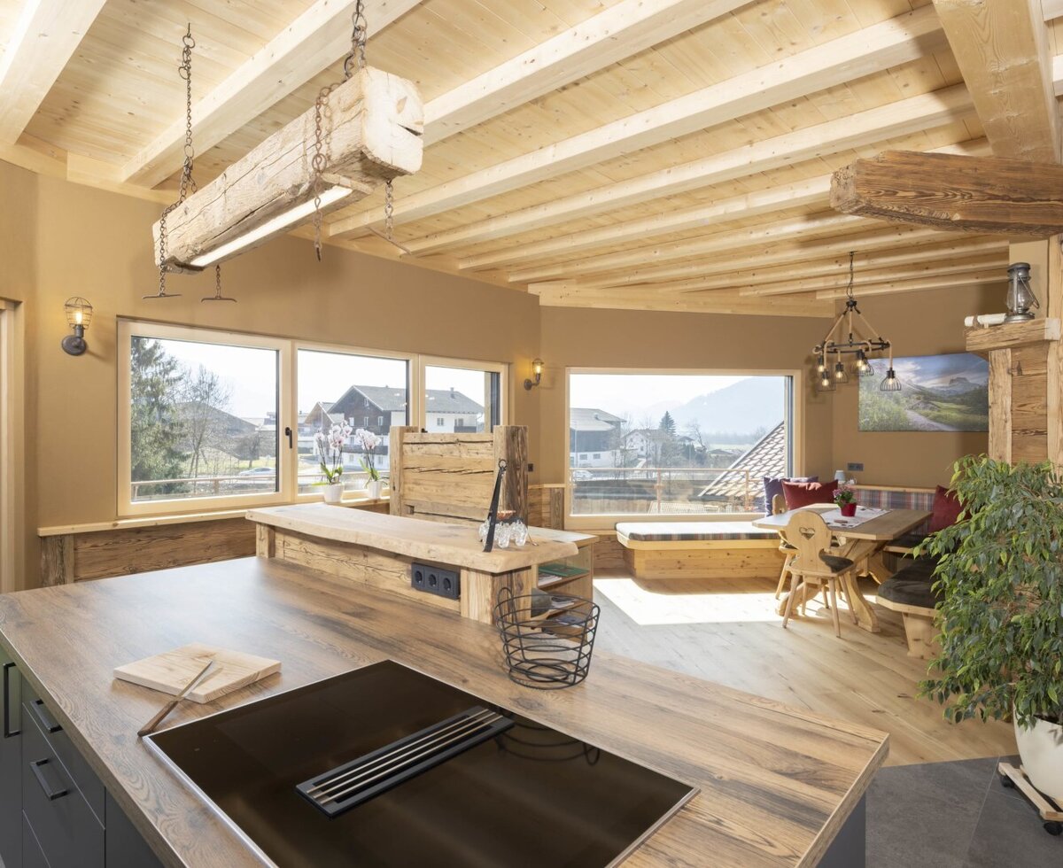 The farm house kitchen and dining area includes a modern induction hob, wooden furnishings, and large windows with views of the surrounding landscape.