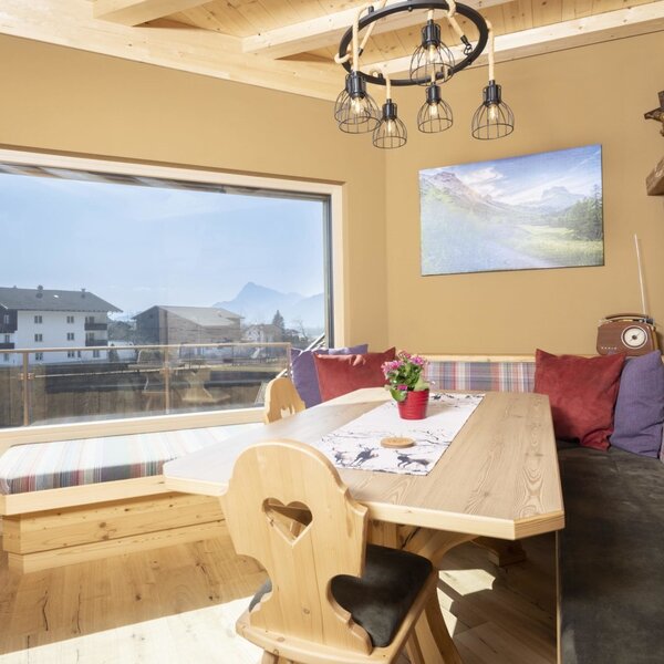The dining area in the Farm House offers a wooden table, corner bench seating, and a large window with views of houses and distant mountains.