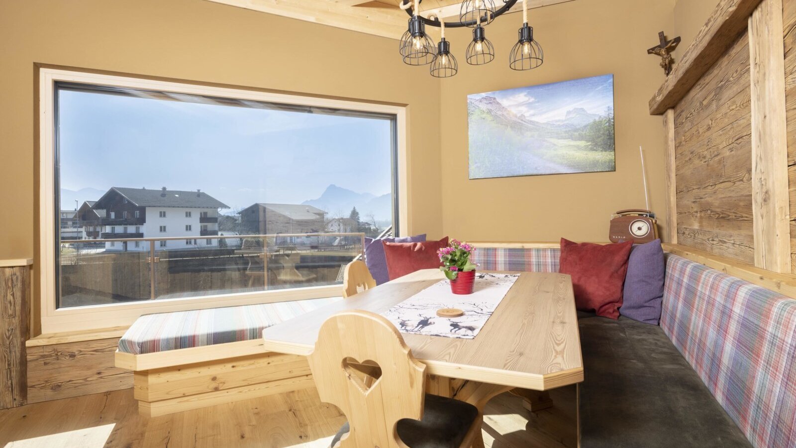 The dining area in the Farm House offers a wooden table, corner bench seating, and a large window with views of houses and distant mountains.