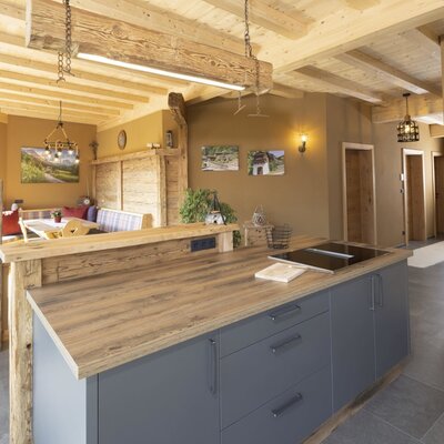 The farm house offers an open-plan kitchen featuring a modern island with an induction hob, adjacent to a dining area with wooden ceiling beams.