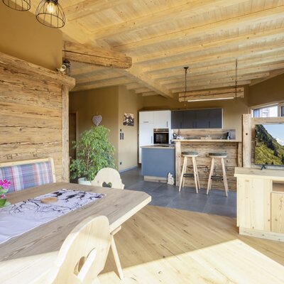 The open-plan living area of the farm house features a wooden dining table with bench seating, a kitchen with a breakfast bar, and a TV entertainment unit.