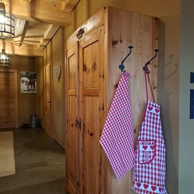 Wooden wardrobe in the farmhouse hallway with hooks holding a red and white checkered tea towel and apron.